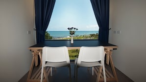 A room with a view of the sea, a wooden table with two white chairs, and a vase with flowers on the window sill. - The Beach Resort & Residence (Pathio)