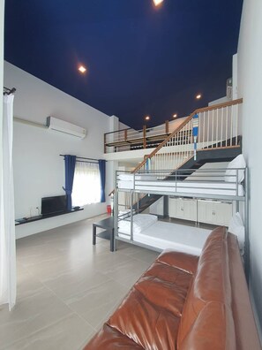 A modern, multi-level room with bunk beds, a staircase, a flat-screen TV, and a sofa.