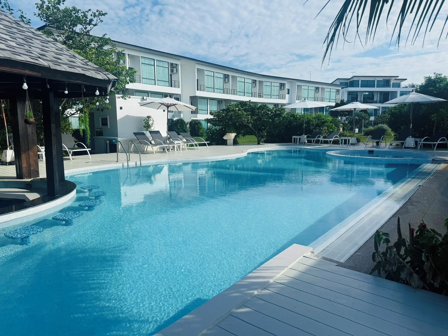 Ein Pool mit Liegestühlen und Sonnenschirmen, umgeben von einem Gebäude mit großen Fenstern.