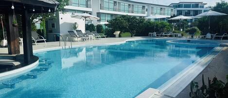 A swimming pool with lounge chairs and umbrellas, surrounded by a building with large windows.