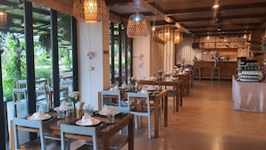A restaurant with wooden tables and chairs, hanging pendant lights, and a bar area in the background. - The Beach Resort & Residence (Pathio)