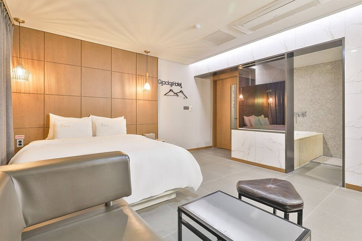 A modern hotel room with a large bed, a seating area, and a bathroom with a vanity and mirror.