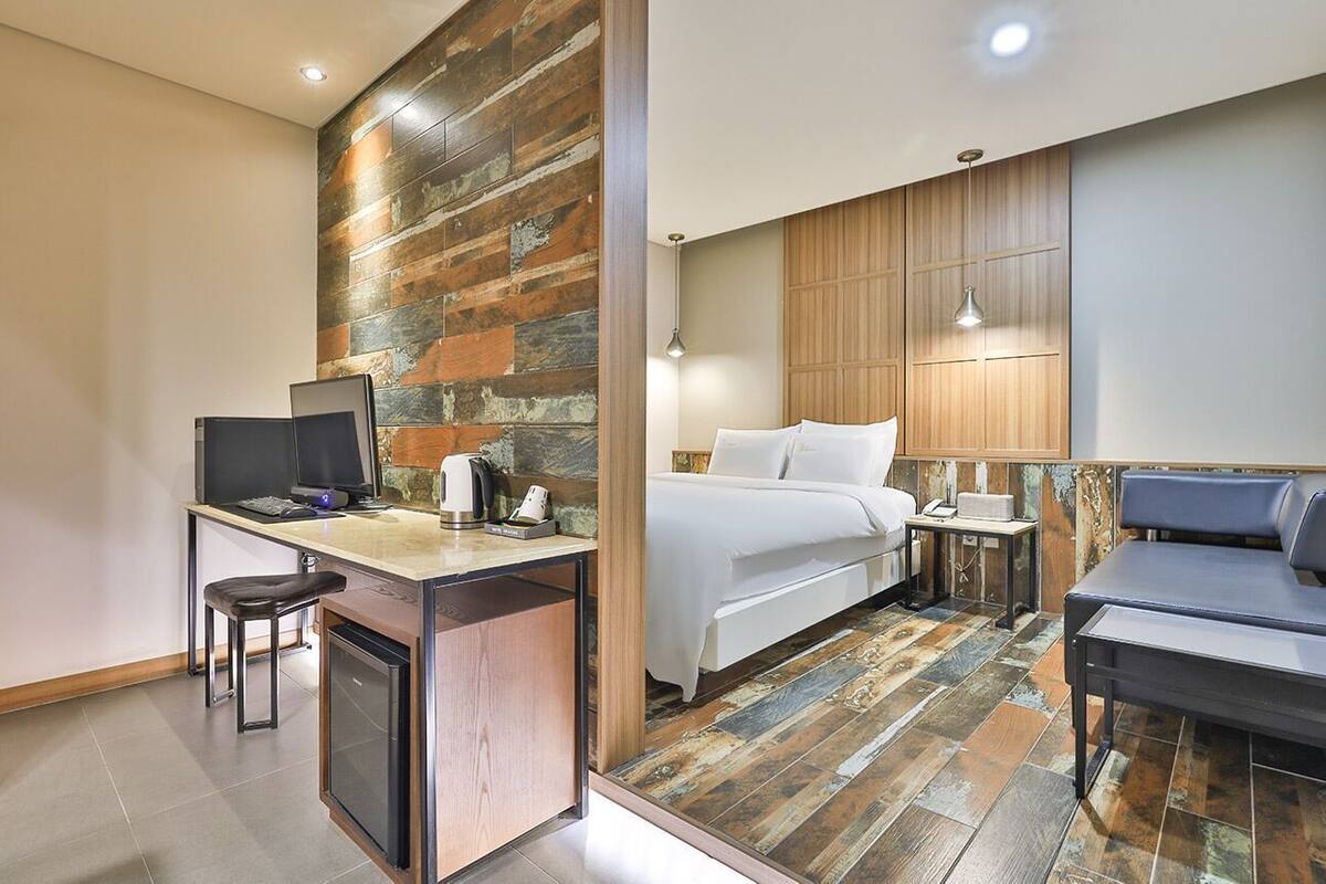A hotel room with a desk, a bed, a sofa, and a wooden accent wall.