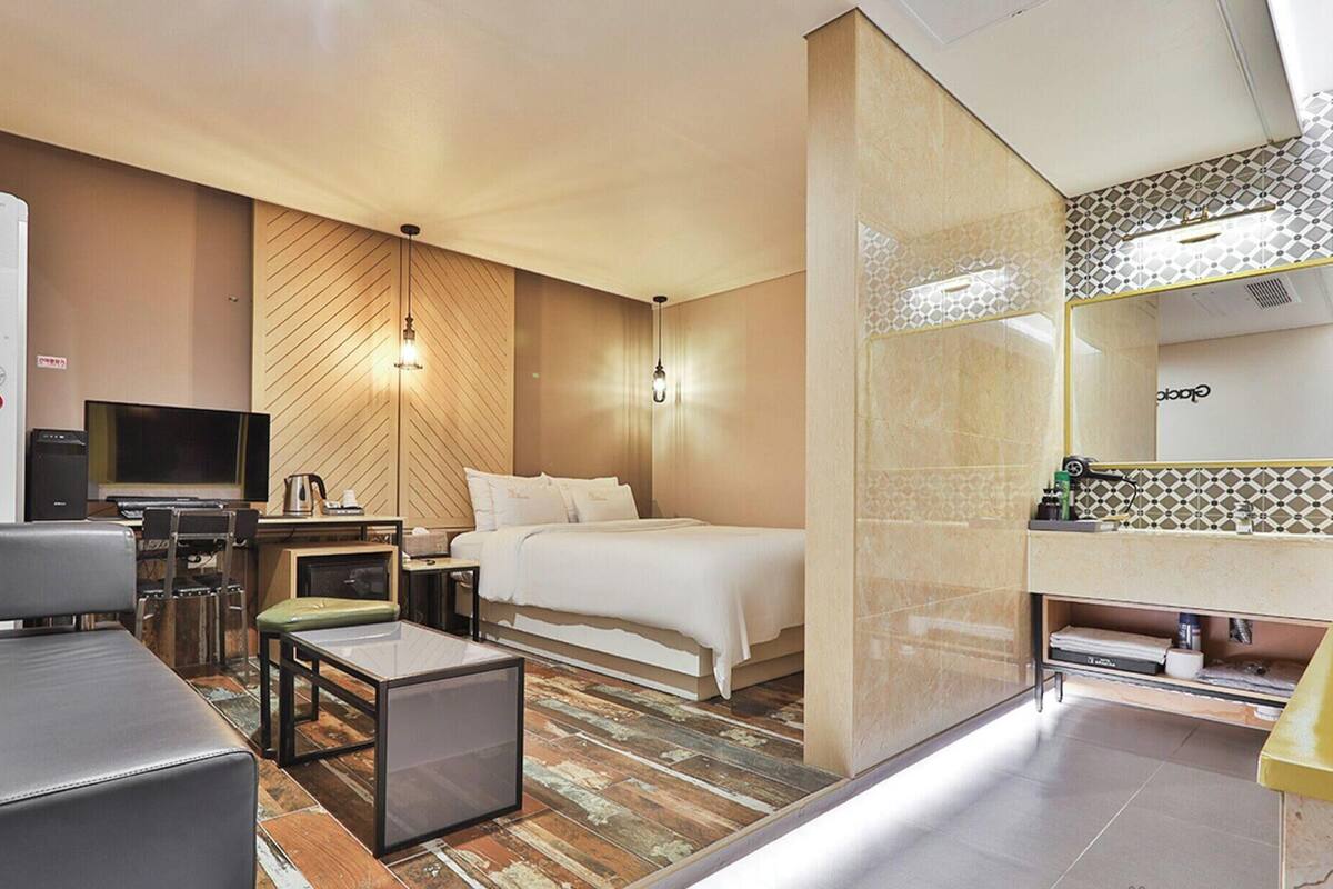 A hotel room with a bed, a desk with a computer, a TV, a seating area, and a bathroom.