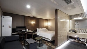 A modern hotel room with a bed, a desk with a computer, a sofa, a small table, and a bathroom with a mirror and toiletries. - Gracias Hotel Gimhae (Gimhae)