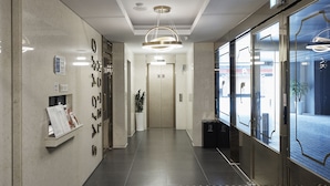 A modern hotel lobby with a geometric patterned floor, a reception desk, and a large glass door leading to the entrance. - Gracias Hotel Gimhae (Gimhae)