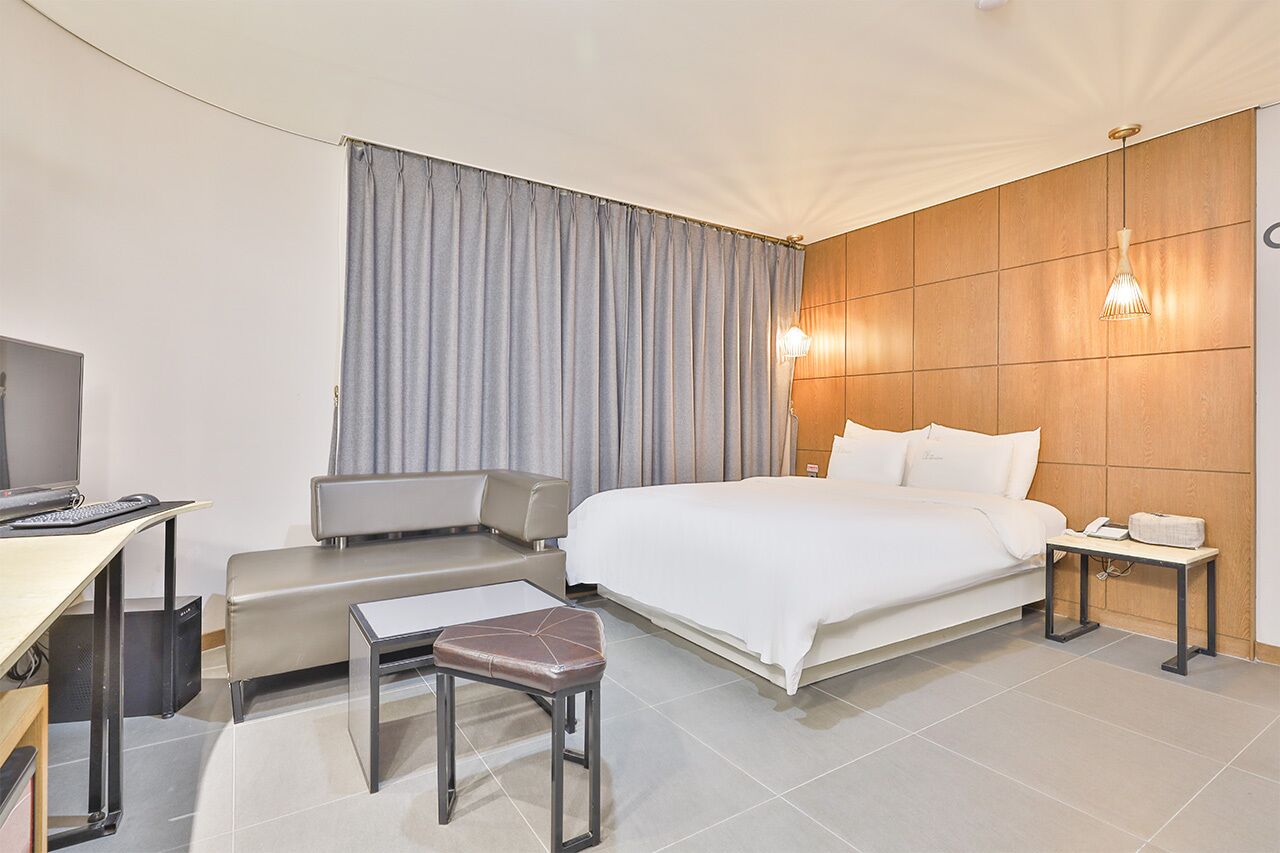 Habitación de hotel con cama, escritorio, silla, banco, televisor y mesita de noche.