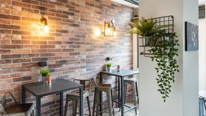 A brick wall with two wall-mounted light fixtures, a hanging plant, and a metal shelf with a potted plant. - co.sleep (Rome)