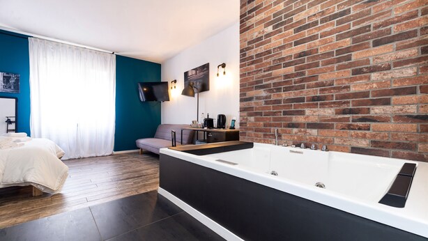 A modern bathroom with a large bathtub, a flat-screen TV mounted on the wall, and a brick accent wall. - co.sleep (Rome)