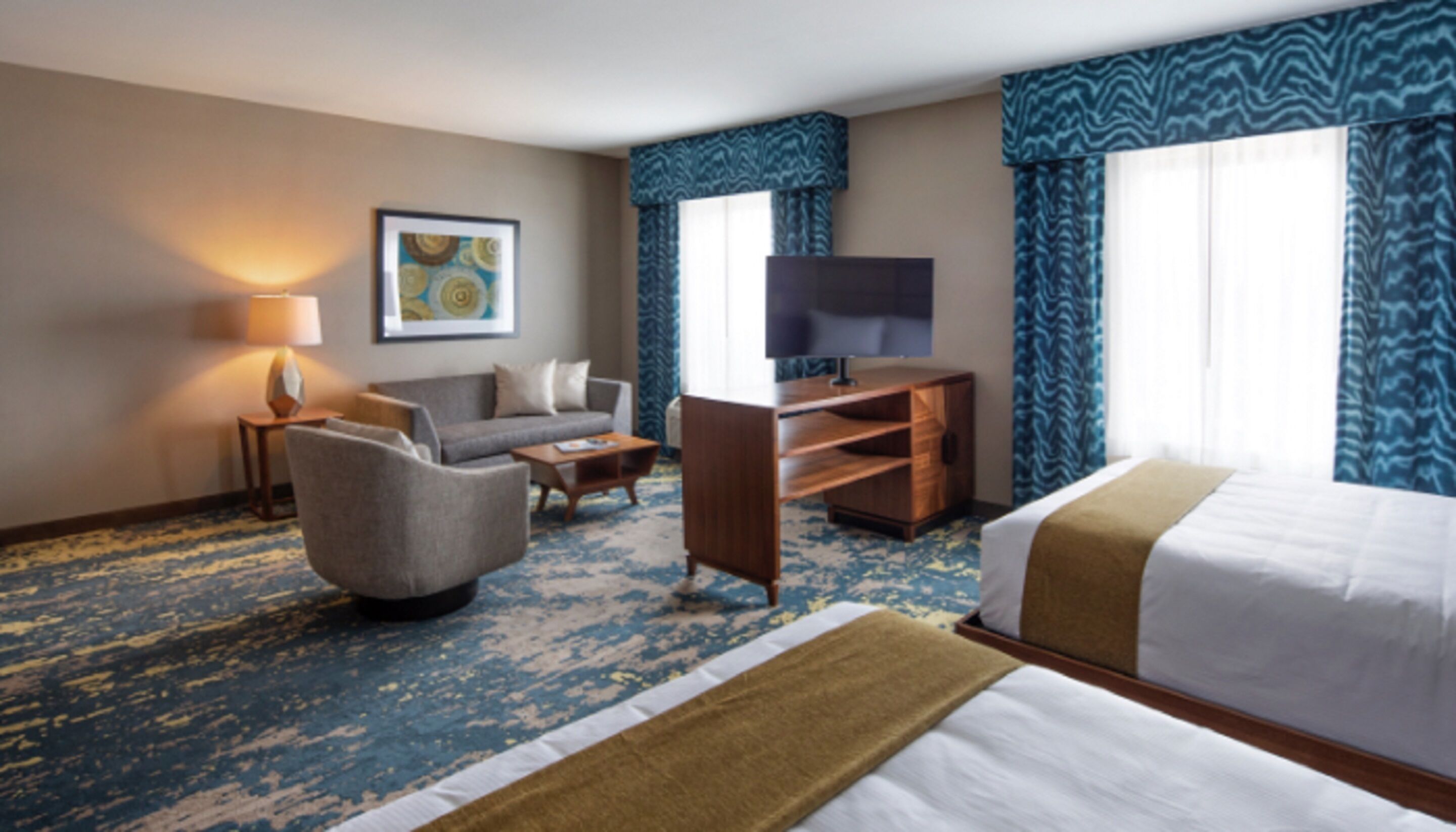 A hotel room with a bed, a sofa, a desk, a television, and a carpeted floor.
