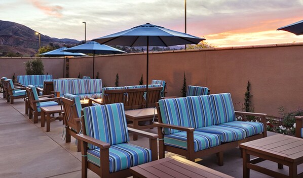Un patio al aire libre con muebles de madera y cojines a rayas azules, con sombrillas y vistas al atardecer.