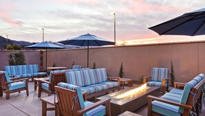 Eine Terrasse im Freien mit gestreiften Sitzmöbeln, einem Feuerkorb und Sonnenschirmen.