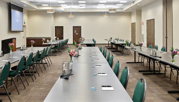 A conference room with long tables, chairs, and a projector screen.