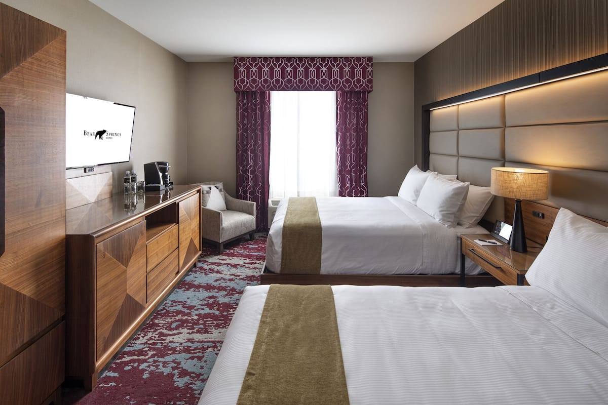 Une chambre d’hôtel avec deux lits, un bureau, une chaise, une télévision et une fenêtre avec des rideaux.
