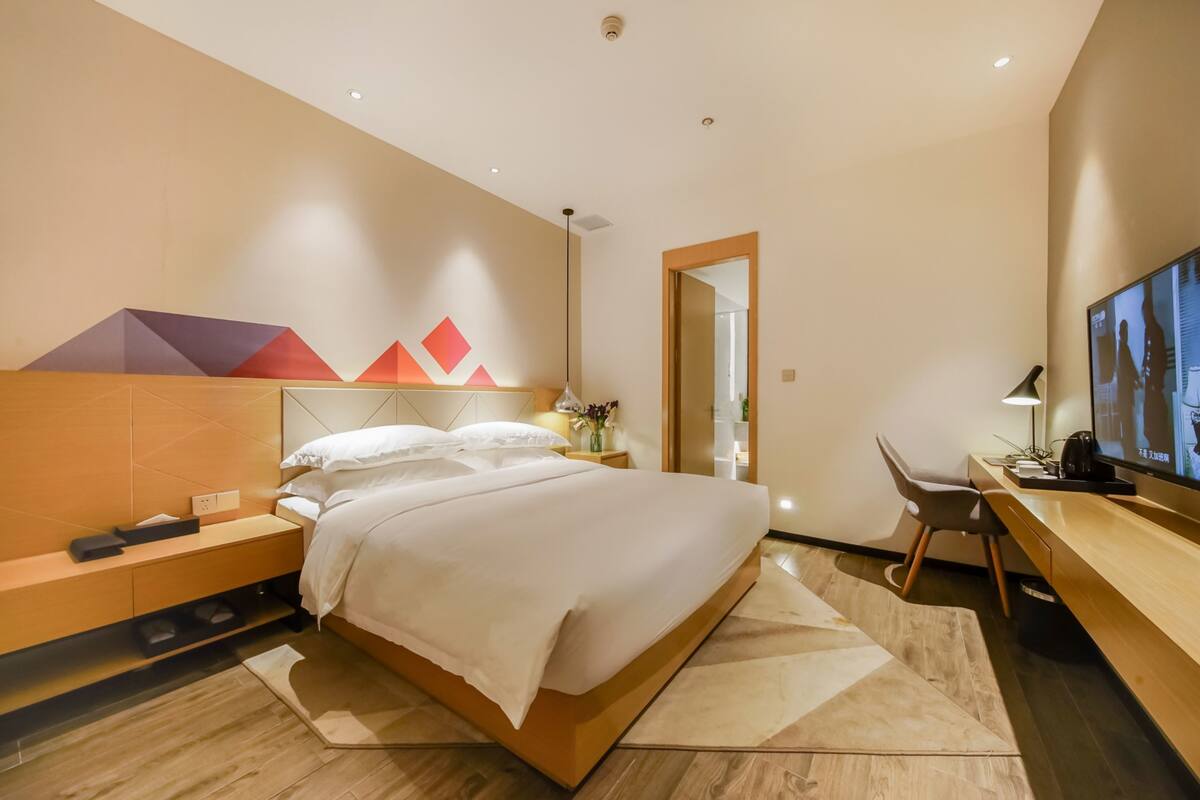 A modern hotel room with a large bed, a desk with a computer, and a TV.