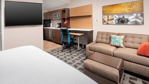 A compact hotel room with a bed, a sofa, a desk with a chair, a flat-screen TV, a microwave, and a coffee maker. - TownePlace Suites by Marriott College Park (College Park)