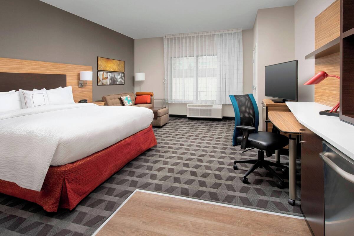 A hotel room with a large bed, a desk with a computer, a chair, and a TV.