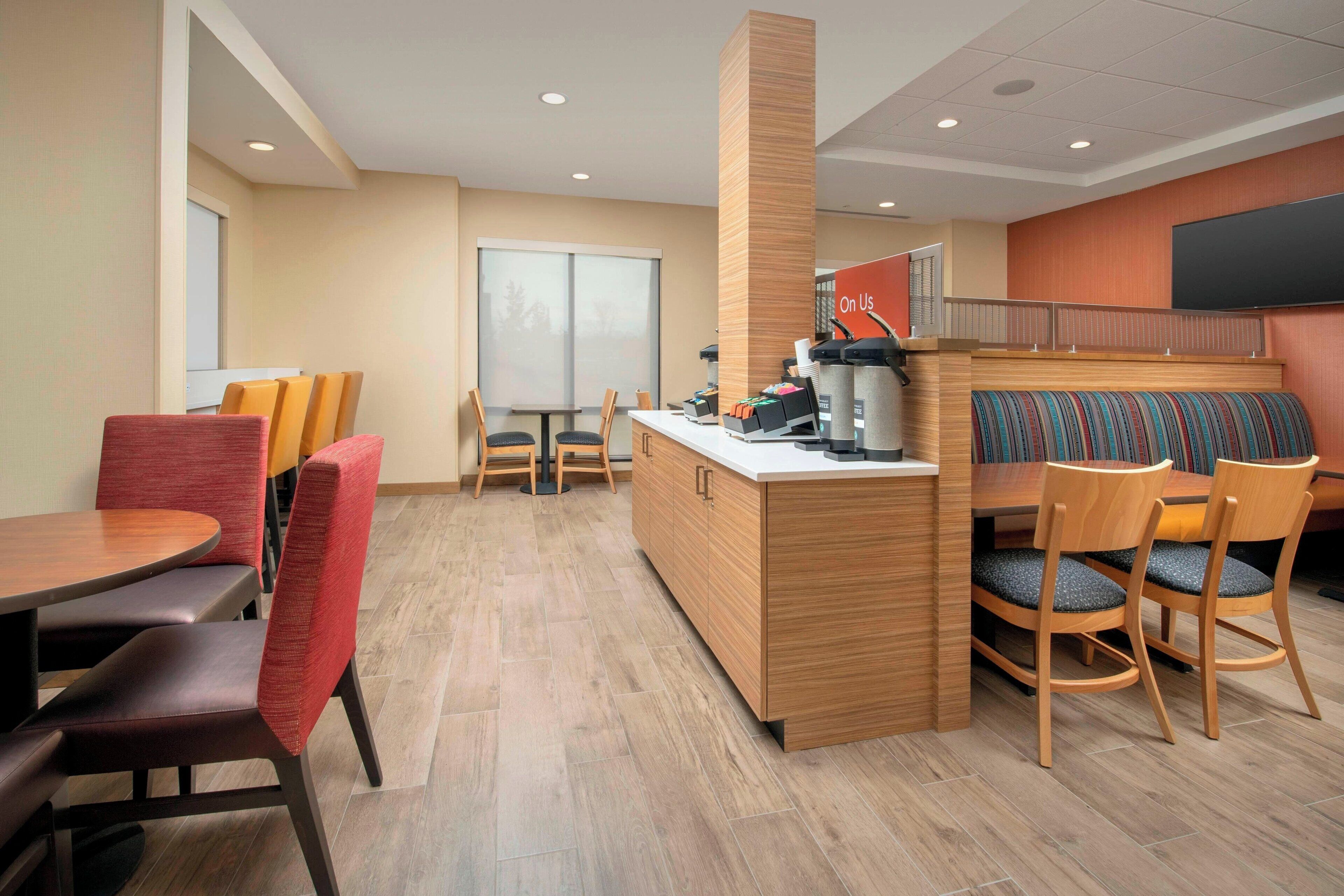 A modern dining area with wooden tables and chairs, a central counter, and a large screen on the wall.