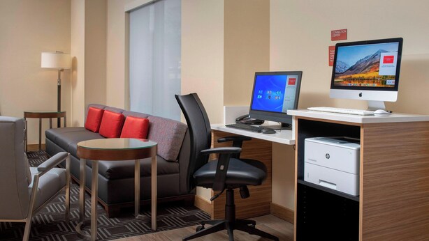 A hotel room with a desk, computer, printer, and a sofa with red cushions. - TownePlace Suites by Marriott College Park (College Park)