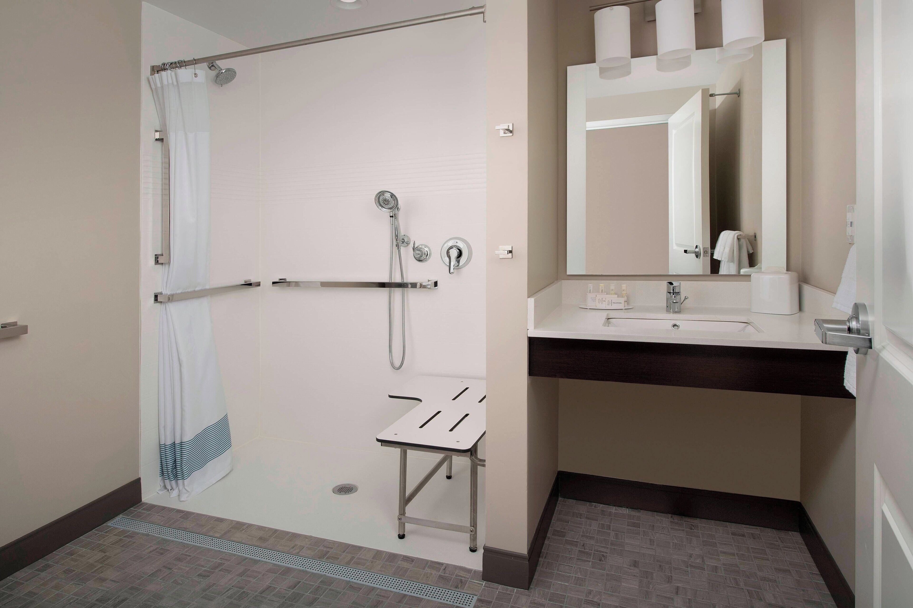 Une salle de bain moderne équipée d’une douche, d’un lavabo, d’un miroir et d’un porte-serviettes.