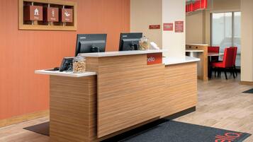 A reception desk with Lenovo computers, a coffee machine, and a jar of snacks. There are red chairs and a table in the background.