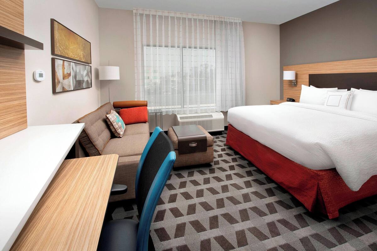 A hotel room with a bed, a desk, a chair, a sofa, and a window with curtains.