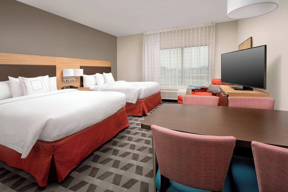 A hotel room with two beds, a TV, a dining table, and a sofa.