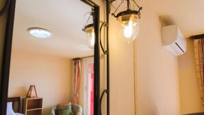 A hotel room with a bed, a chair, a small table, a mirror, and a ceiling light fixture.