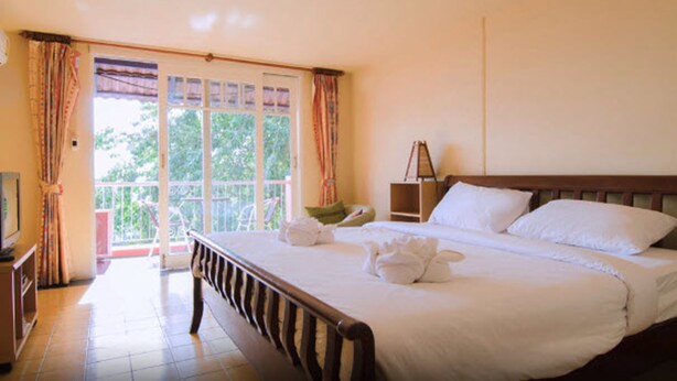 A hotel room with a bed, a television, a bedside table, and a balcony with curtains.