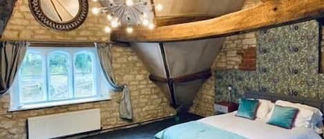 A bedroom with a sloped ceiling, a bed with blue bedding, a window with curtains, and a decorative light fixture.