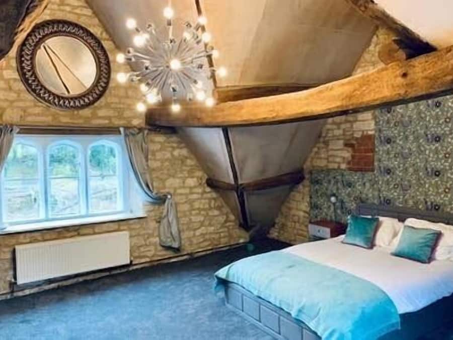 Un dormitori amb sostre inclinat, un llit amb roba de llit blava, una finestra amb cortines i una làmpada decorativa.