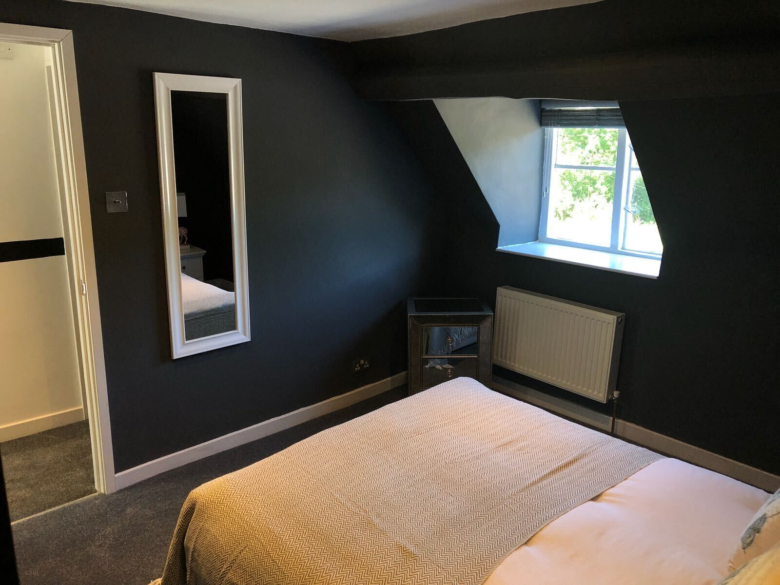 Une chambre à coucher avec un lit, une fenêtre, un radiateur et un miroir.