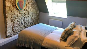 A bedroom with a stone wall, a bed with a patterned blanket, and a window with a view.