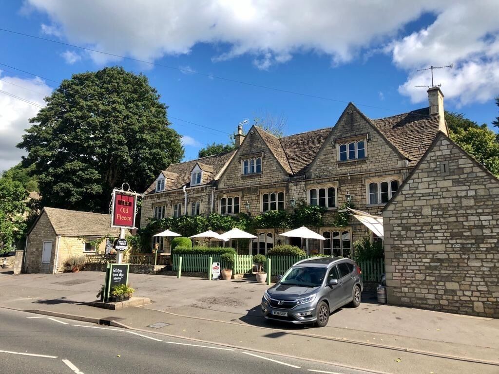 A stone building with a sign for 'The Old Fleece' pub, a parked car, and a clear sky.
