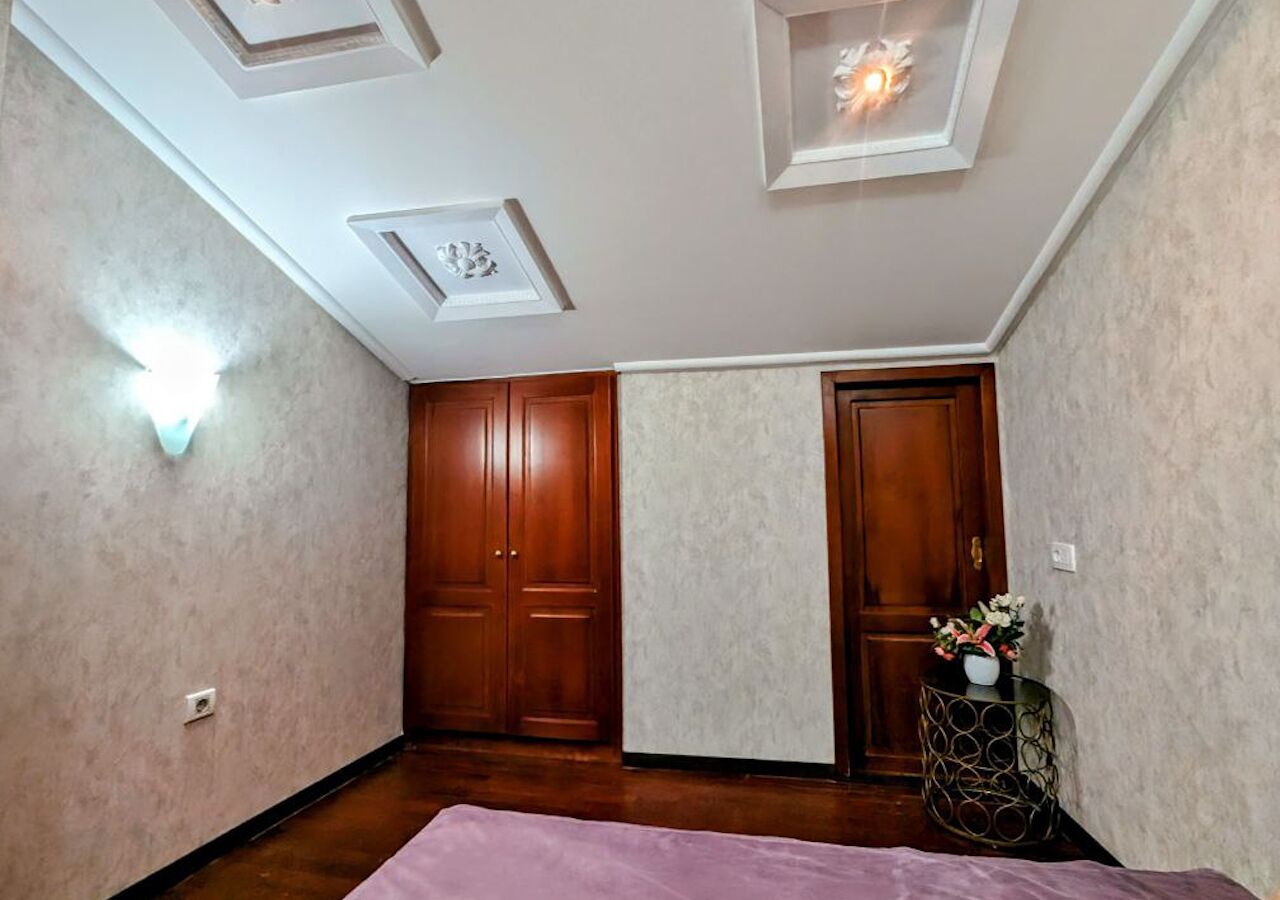 Een kamer met een houten garderobe, een bed met een roze sprei en een ronde tafel met een potplant.
