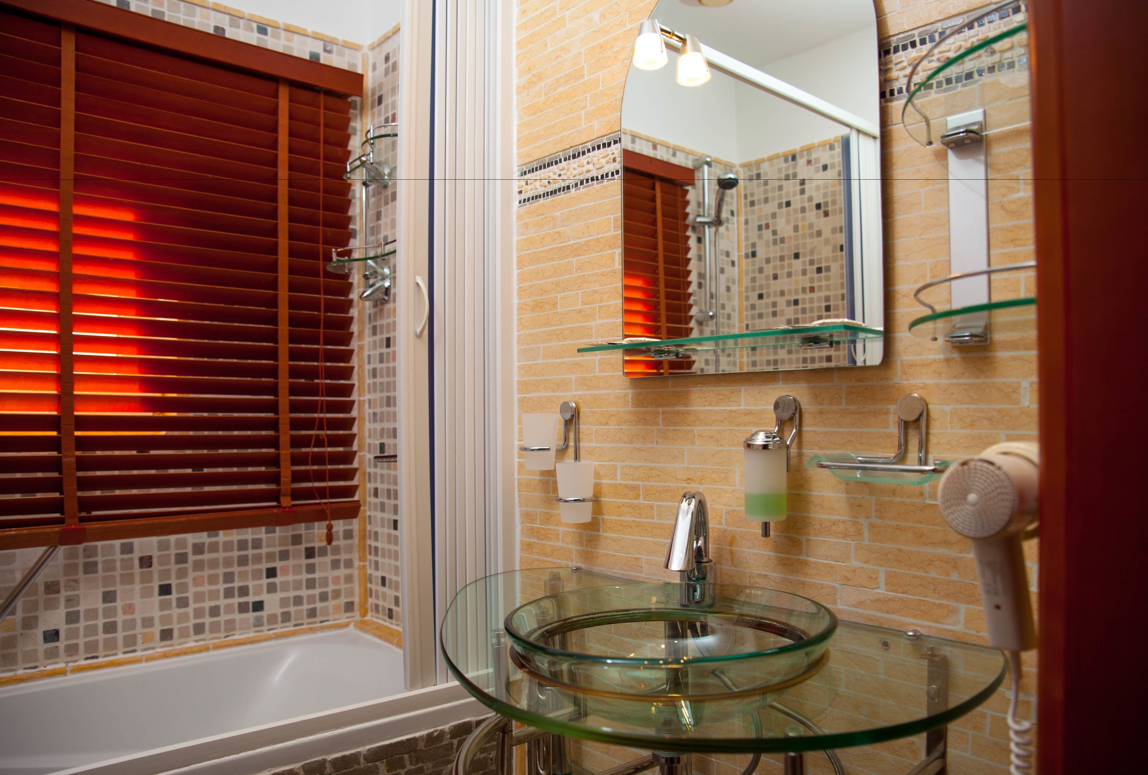Un baño con un lavabo de vidrio, ducha y espejo.