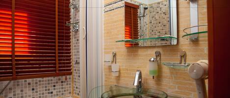 Un baño con un lavabo de vidrio, ducha y espejo.