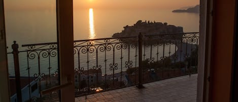 Balcón con vista al mar al atardecer, destacando un islote rocoso a lo lejos.