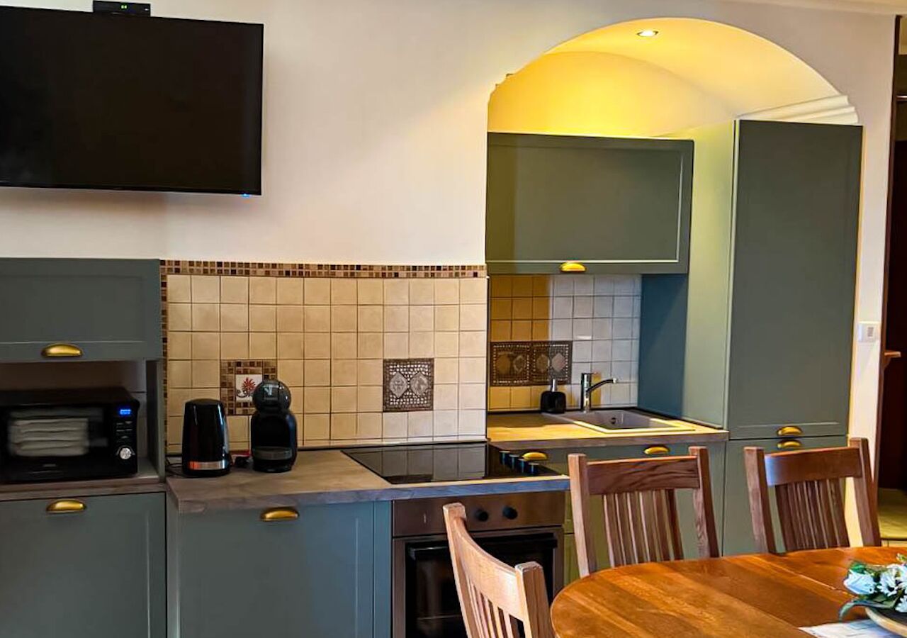A compact kitchen with a microwave, coffee maker, and toaster. There is a dining table with chairs and a TV mounted above the counter.