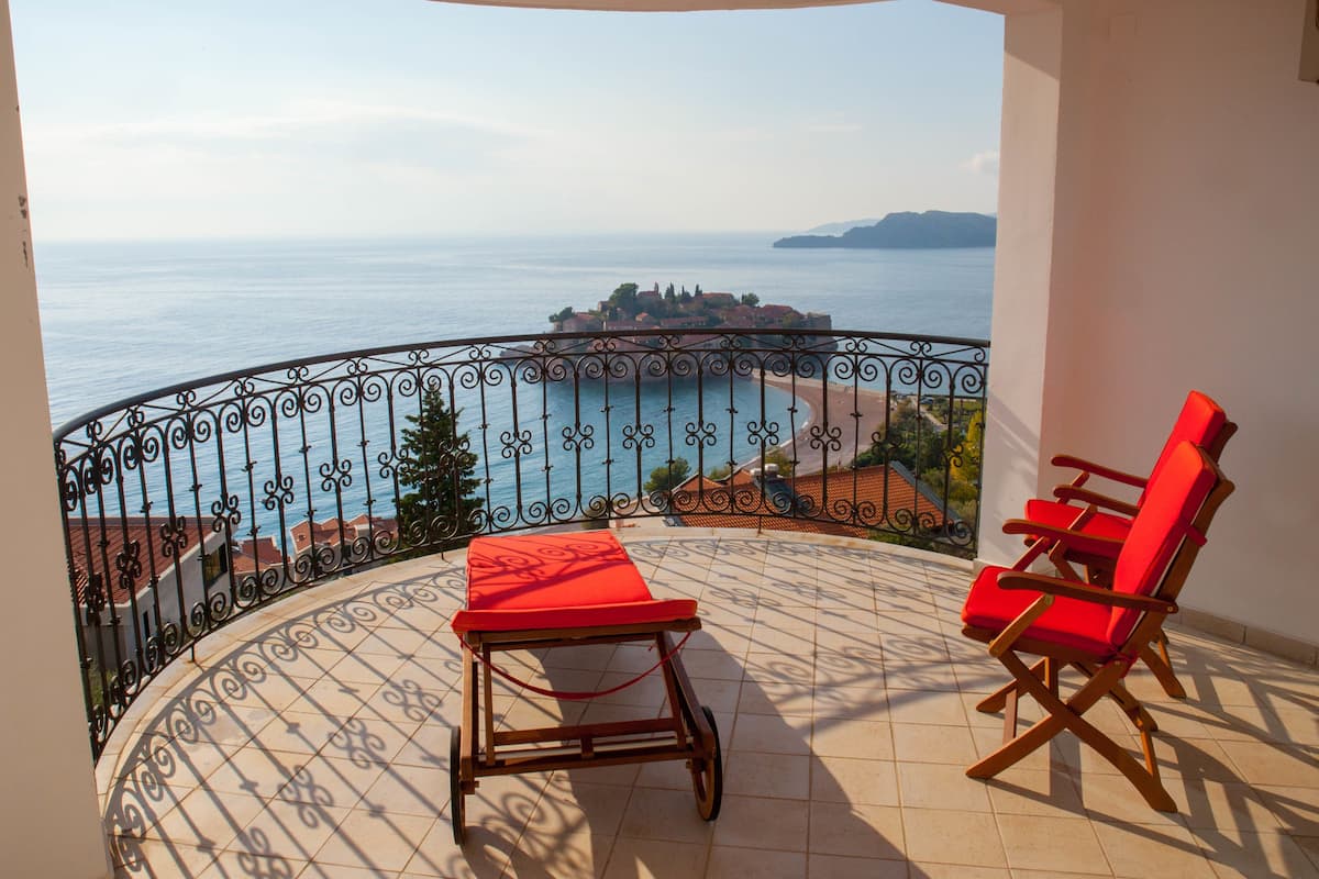 Ein Balkon mit Meerblick, ein Tisch mit rotem Kissen und zwei rote Stühle.