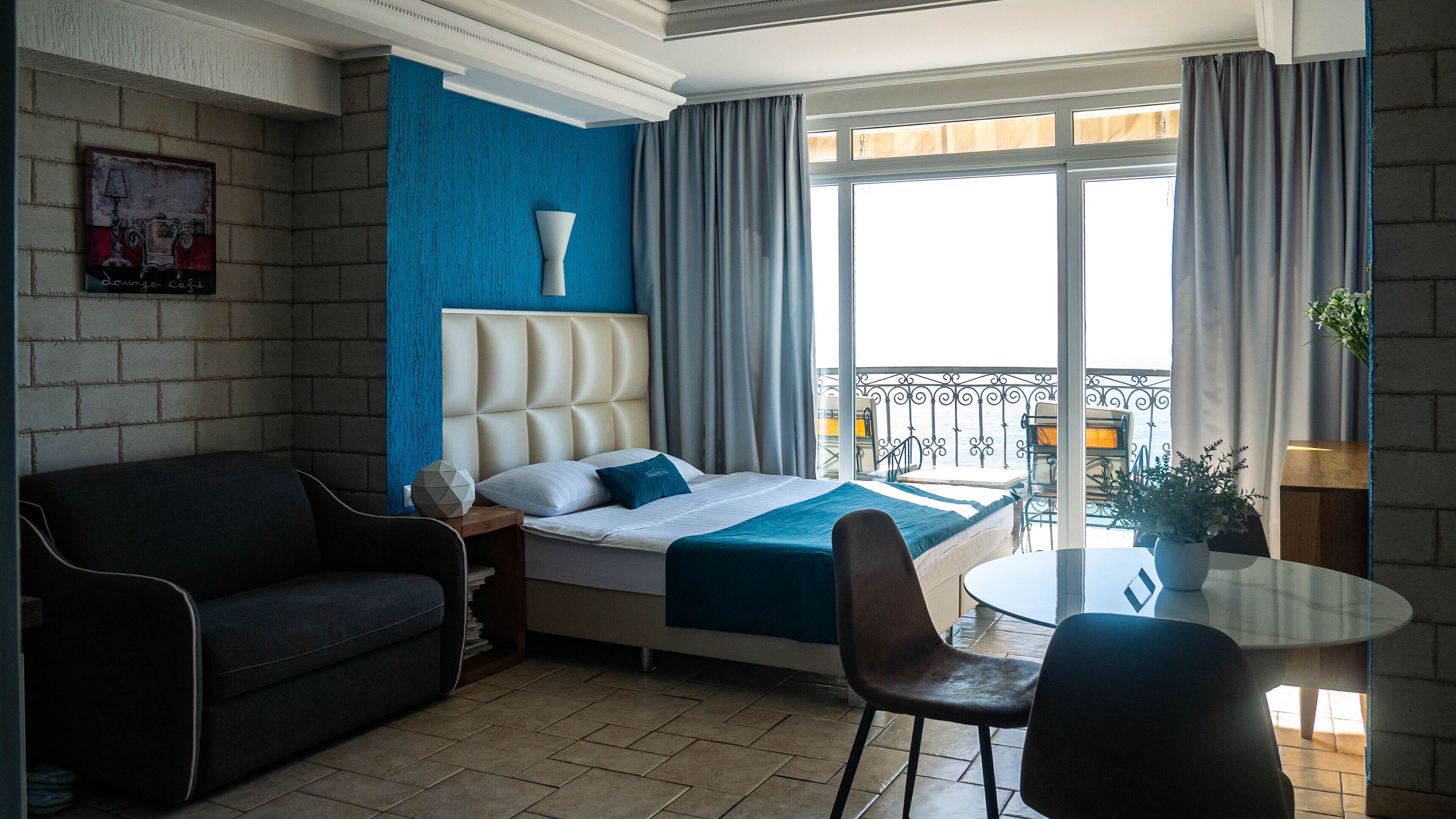 Habitación de hotel con cama, sofá, mesa de comedor y balcón con vistas.