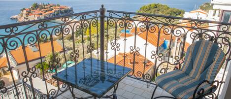 A balcony with a table and chairs, overlooking a coastal town and the sea.
