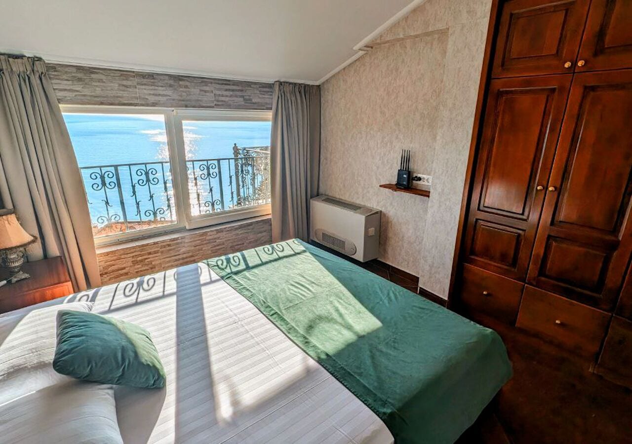 A hotel room with a bed, a view of the sea, and a balcony.