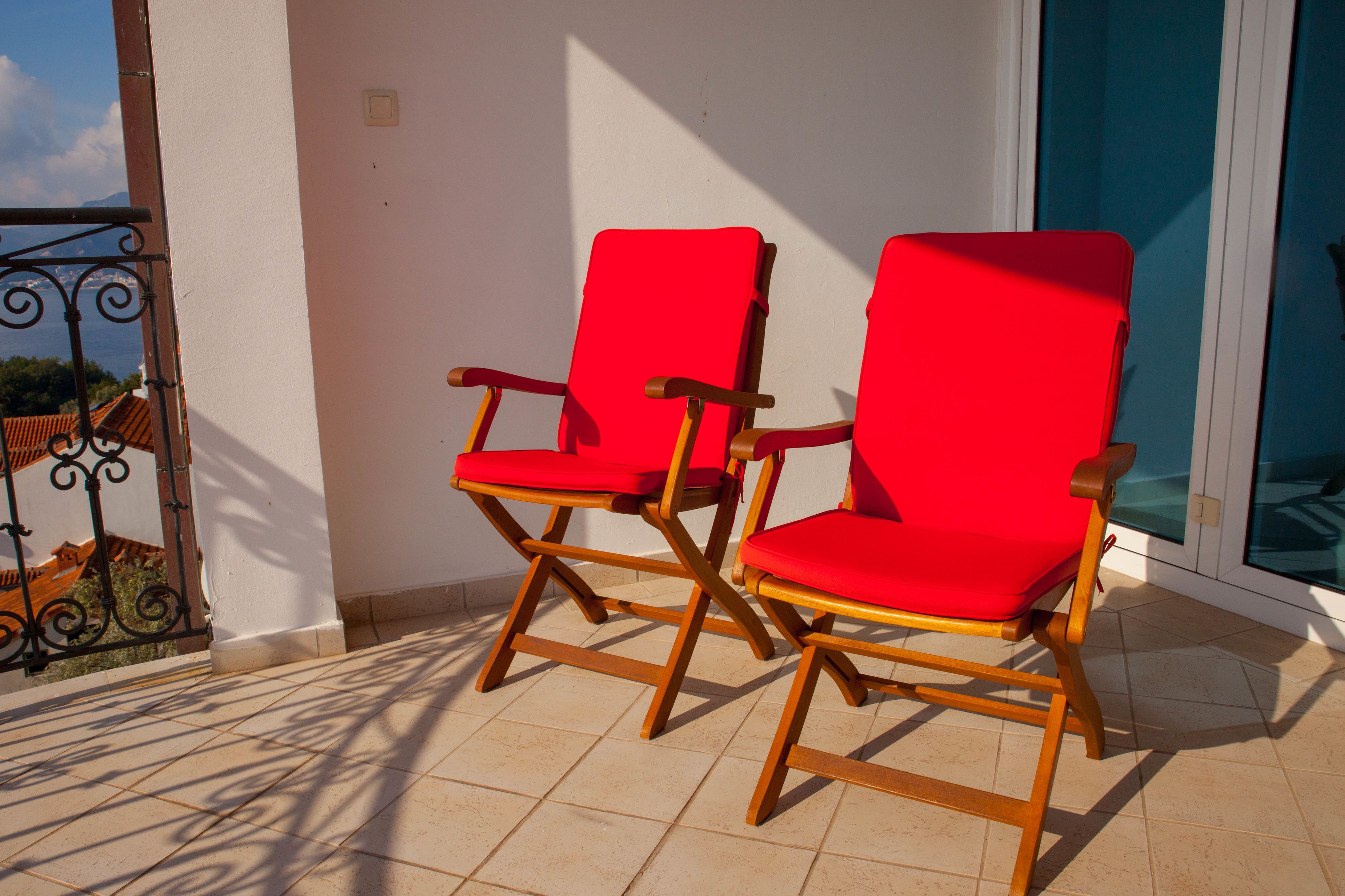 Twee rode stoelen met houten frame op een balkon met betegelde vloer.