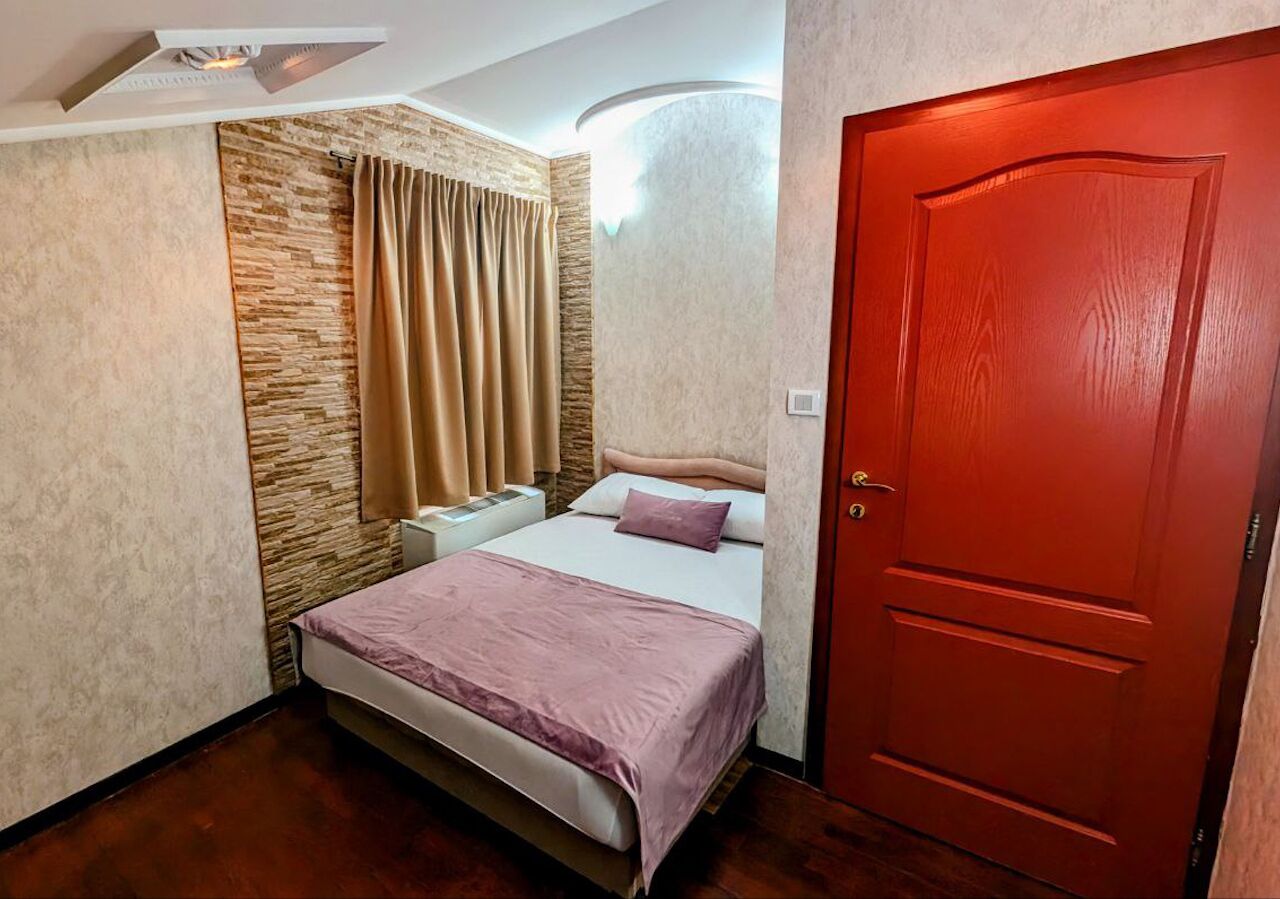 A small, cozy bedroom with a bed, a nightstand, a red door, and a stone accent wall.