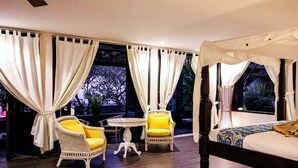 A bedroom with a canopy bed, a small round table, two chairs, and a view of trees through the windows. - Le Mirage Villa Santai (Sukasada)
