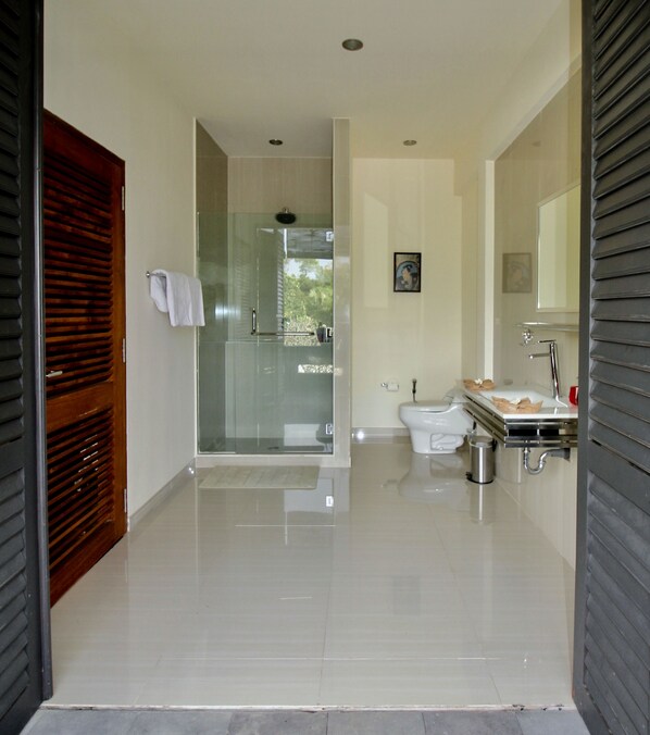 A modern bathroom with a glass shower enclosure, a toilet, and a sink with a mirror. - Le Mirage Villa Santai (Sukasada)