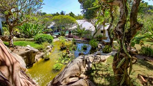 A garden with a pond, various plants, and a rustic stone structure. - Le Mirage Villa Santai (Sukasada)