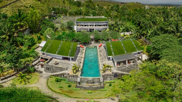 A resort with a central swimming pool, multiple green-roofed structures, and lush surrounding vegetation. - Le Mirage Villa Santai (Sukasada)