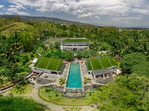 A resort with a central swimming pool, multiple green-roofed structures, and lush surrounding vegetation. - Le Mirage Villa Santai (Sukasada)